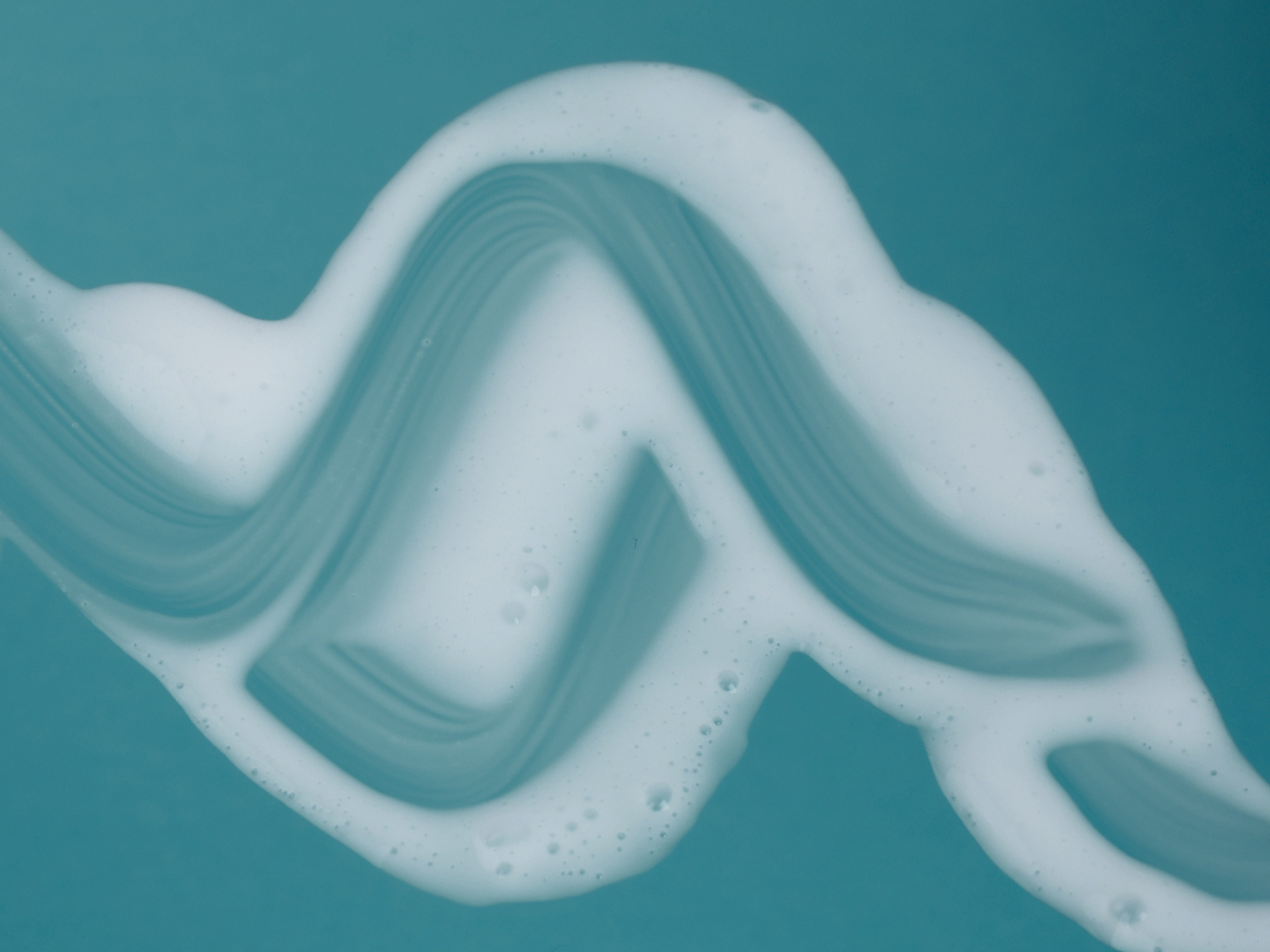 Macro view of the smooth white S.H.I.E.L.D. moisturizing gel cream texture on a teal background.