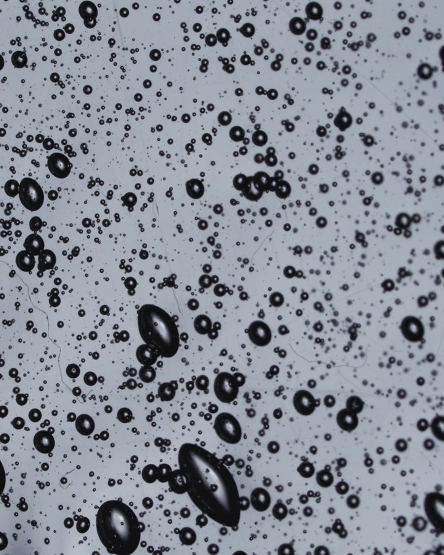 Close-up abstract view of the E.Q.U.I.N.O.X. hydrating cleanser texture with water droplets and micro-bubbles.